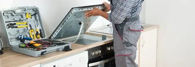 Cooktop repair technician lifting a built-in stovetop for service in Baton Rouge, LA