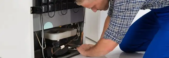 Refrigerator repair technician servicing the compressor and condenser area in Baton Rouge, LA