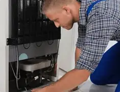 Refrigerator repair technician servicing the compressor and condenser area in Baton Rouge, LA